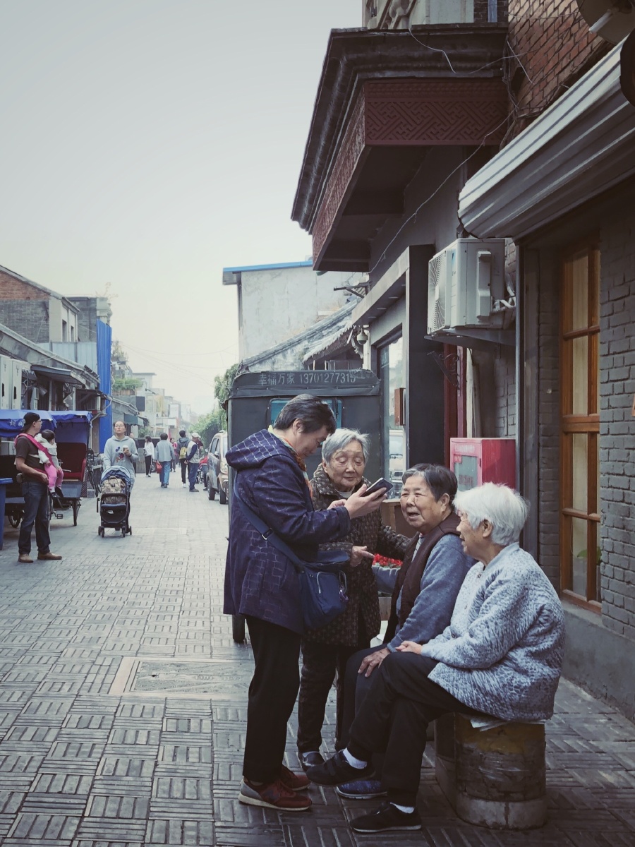 北京的老胡同里,一位大妈在给邻居们分享她的大孙子照片