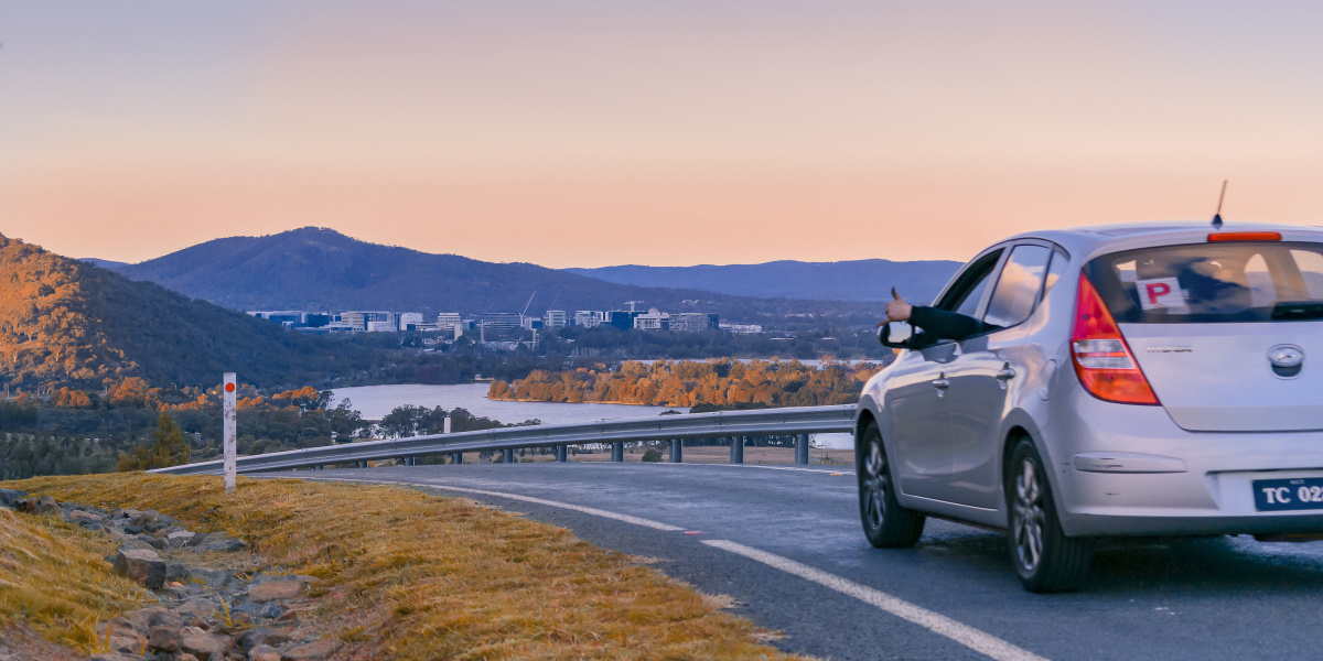 夕阳下一辆银色汽车行驶在山路上,远处有河流和树林