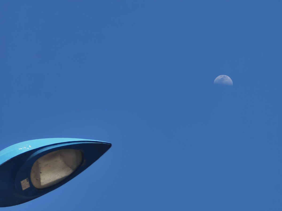 大晴天,抬头发现一路灯上的天空中半个月亮也嵌在蓝天里,手机长焦端随