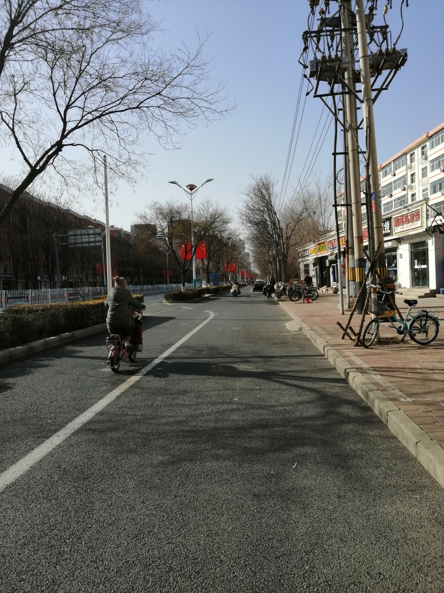 北方城市沧州的街头一景有骑自行车的行人有道路清扫车有小区楼房还有