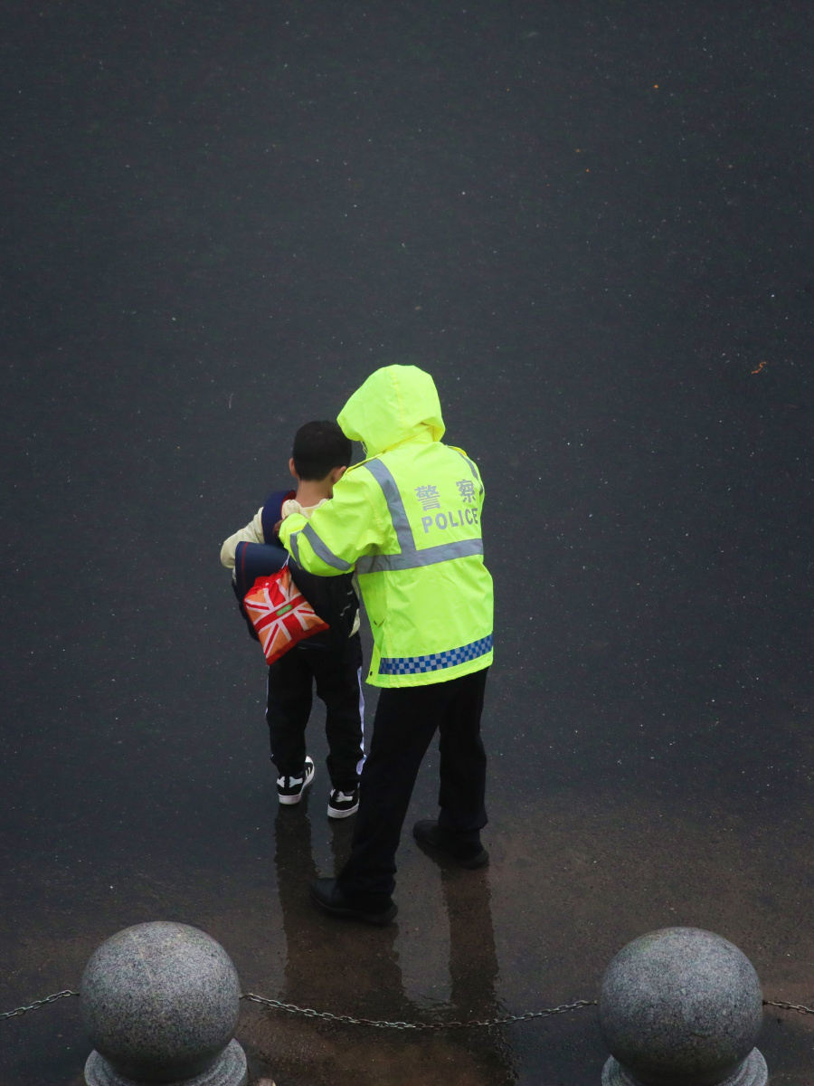 雨中的温暖:一位警察帮助小朋友过马路,然后又帮助整理一下书包.