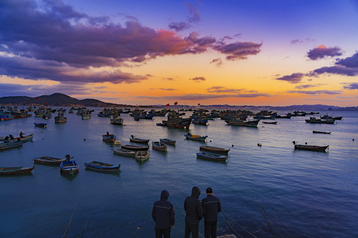 威海冬日傍晚晚霞映红天际渔船停靠岸边几杆海钓的渔者