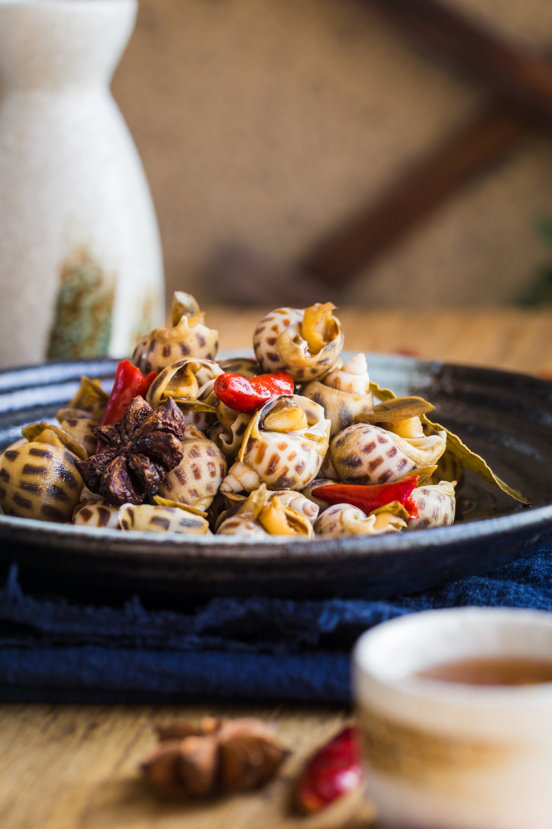 木制桌面上的辣卤花螺配梅子酒