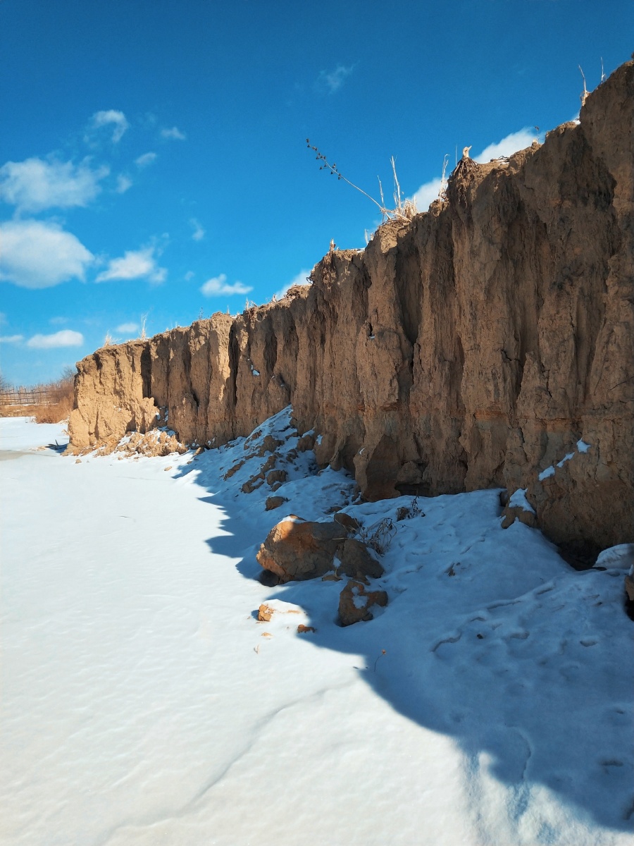 冰冻的小河上落着厚厚的雪岸边陡峭蓝天上飘着几朵白云