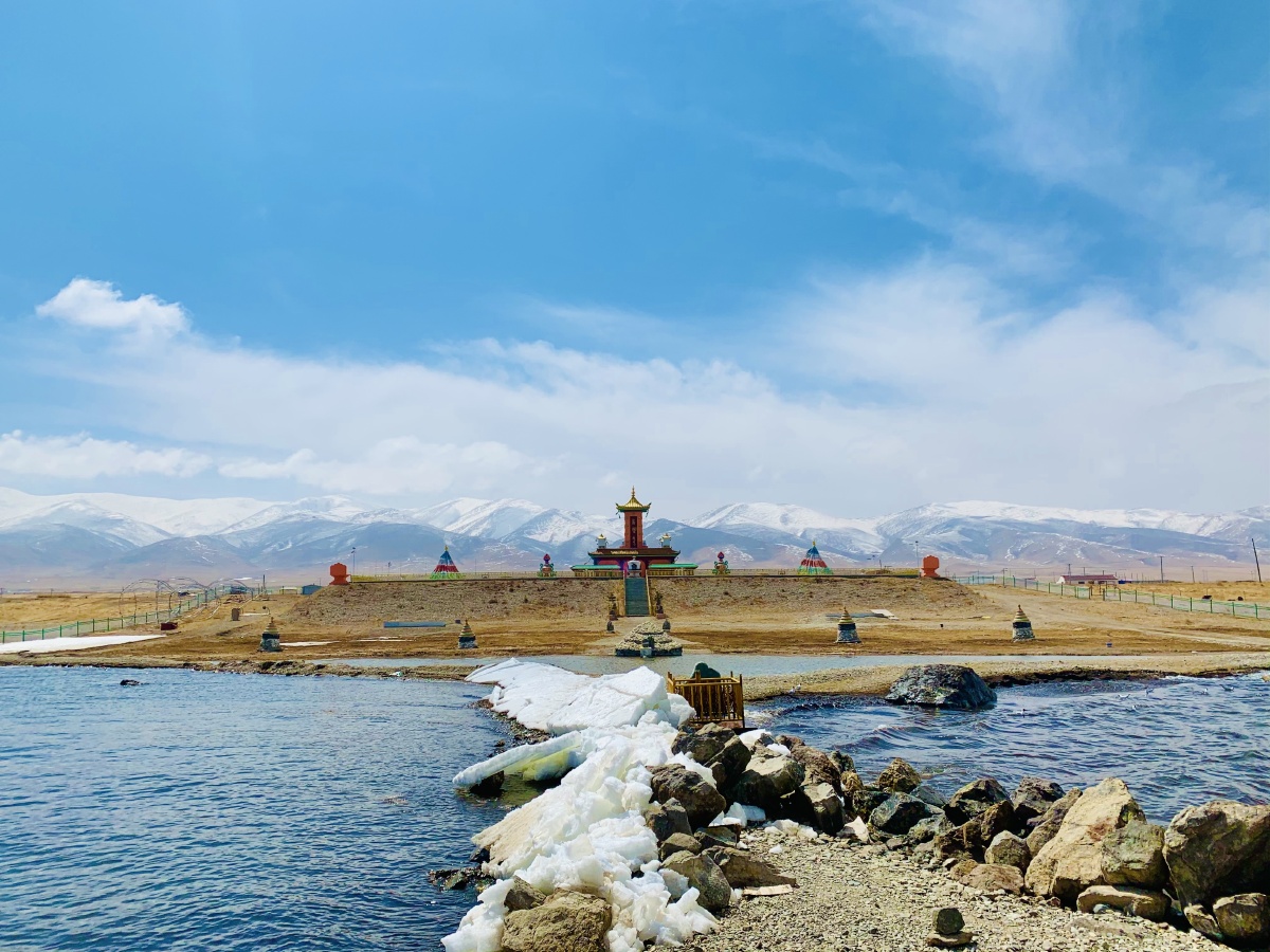 青海湖边通向湖水中的陆地,转身背后是延绵的雪山和岸边巍峨的龙王庙