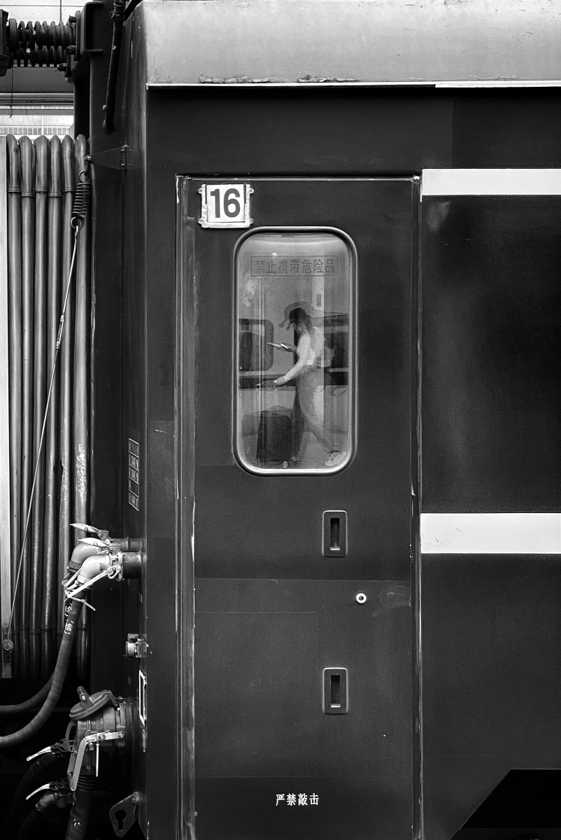 《月台》月台上有旅客路过,倒影在停在月台上的绿皮火车的玻璃窗里