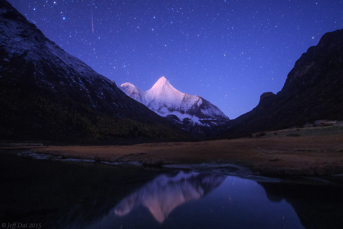 沐浴在黎明曙光中的央迈勇雪峰,一颗猎户座流星划破天际.