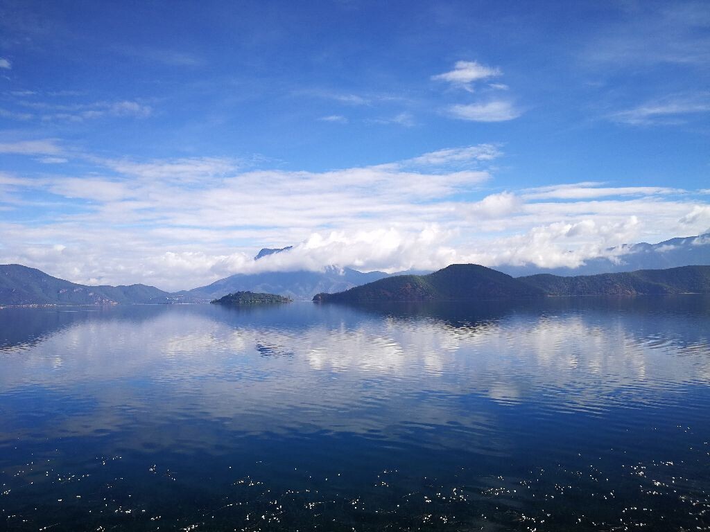 骑自行车环湖,在浪放村村拍摄的泸沽湖,湖中的小岛是里务比岛。湖面倒映着蓝天白云,水性杨花缠绕在湖边。