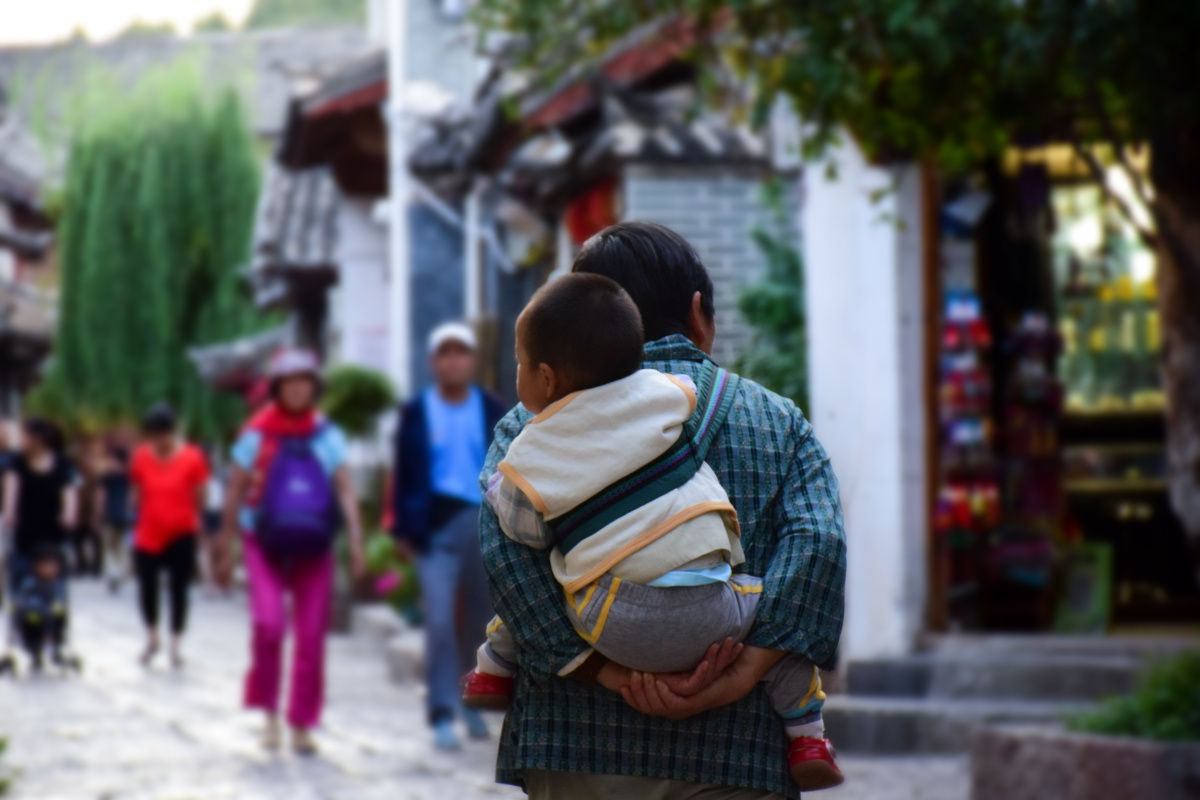 老奶奶背着自己的小孙子,小孙子在奶奶背上看着来来往往的人群,使人