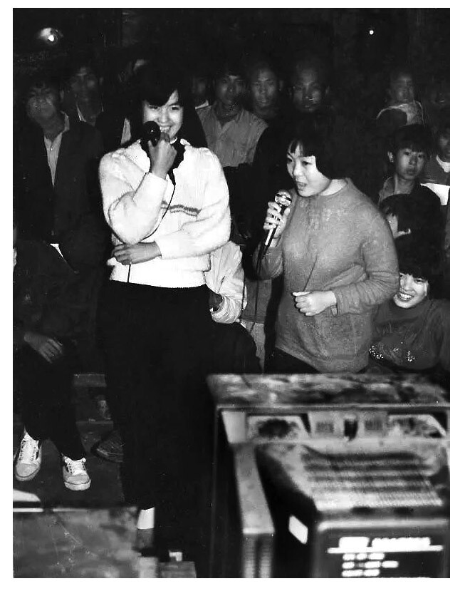 摄于1990年左右，江西安远县。刚刚风行起来的卡拉OK，一毛钱唱一首。街头的姑娘还有些羞涩，无聊的逛街人群围观犹如看演出。凤凰205，乐凯胶片拍摄