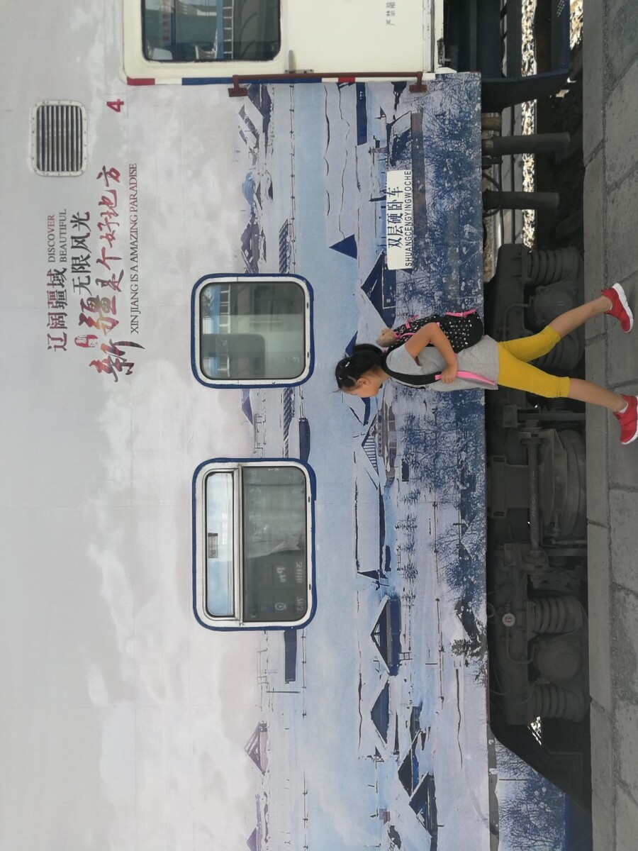 小旅客从旅游专列下车并经过大幅车身广告。这是新疆依托火车开通之后推出的周末旅游专列，火车联通南北疆，城与城之间可以方便的串门子。