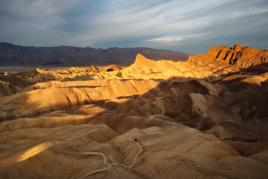 加州死亡谷Death Valley的Zabriskie Point。这天早上的日出朝霞异常绚烂。当太阳躲到云后时大家以为早上的光线盛宴结束了。哪料到之后突然有一刻，阳光穿过了云隙，金色的洒在了奇特的地貌上，一切都显得这么大气。而此时刚好一位游客在往前走，我等他走进了镜头里捕捉了这一刻。让人不禁感叹，天地广袤，苍茫一瞬间。