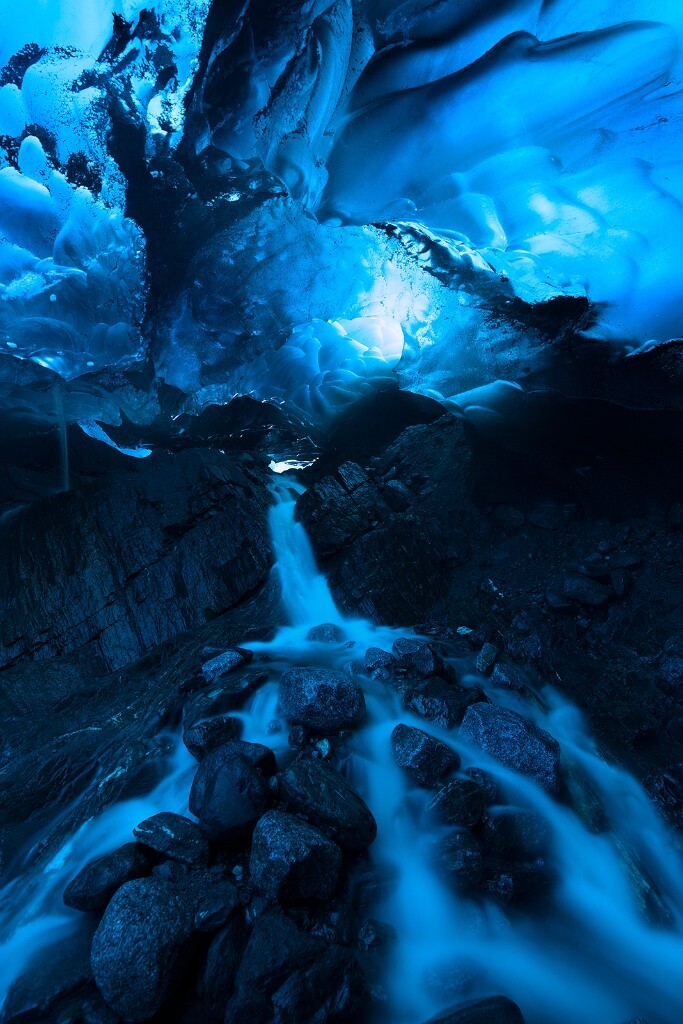 这是阿拉斯加冰洞之旅的第二张。冰洞后段的融化，反而在冰洞深处形成了另一个神秘空间。往冰洞内部走，我们发现了一个瀑布，顺着瀑布边攀爬下来，里面别有洞天。而回身一望，便是如此精彩的画面。在冰洞顶部的幽幽蓝光下，溪水激流而落，宛如蛟龙入洞。
