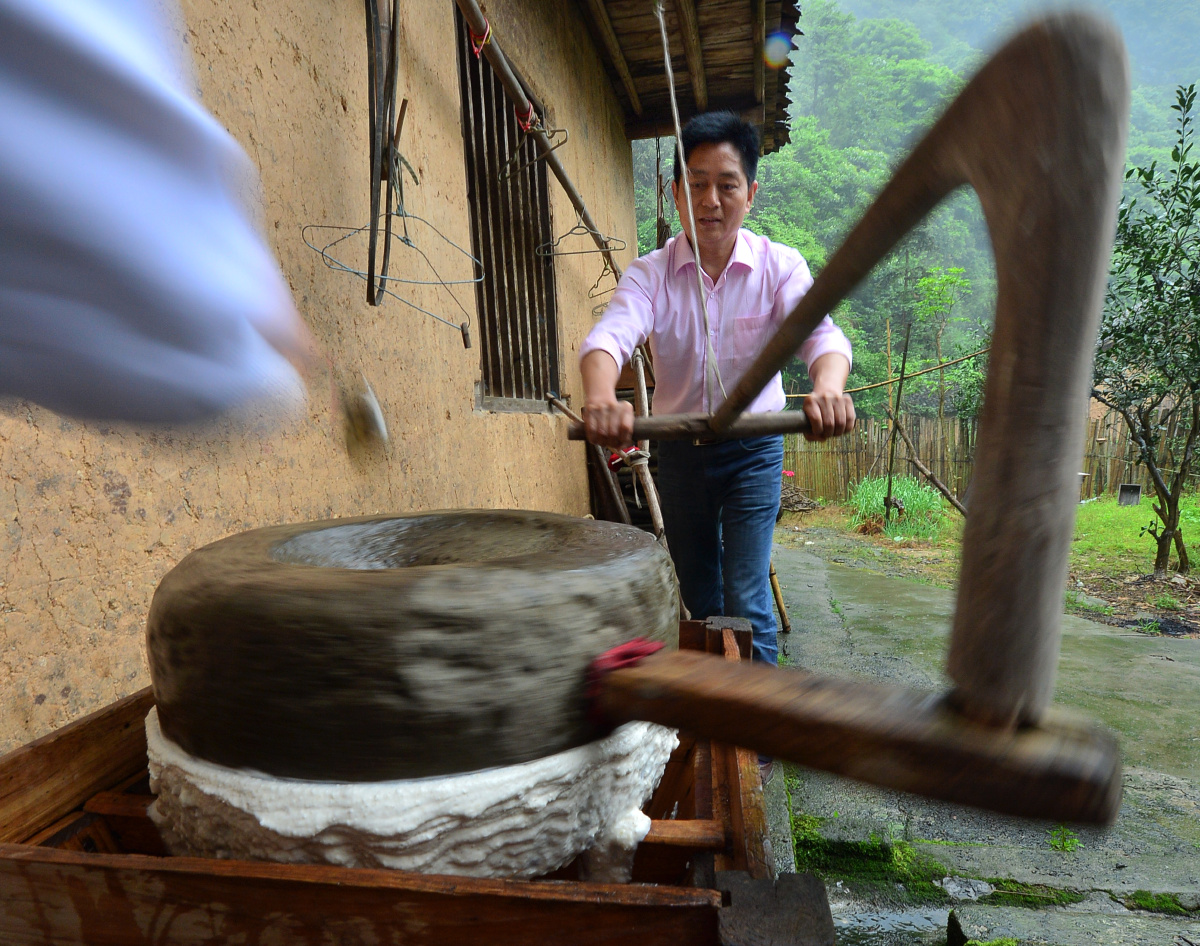 曾祥志夫妇俩一个往磨眼里添黄豆,一个持着手拐推磨盘.