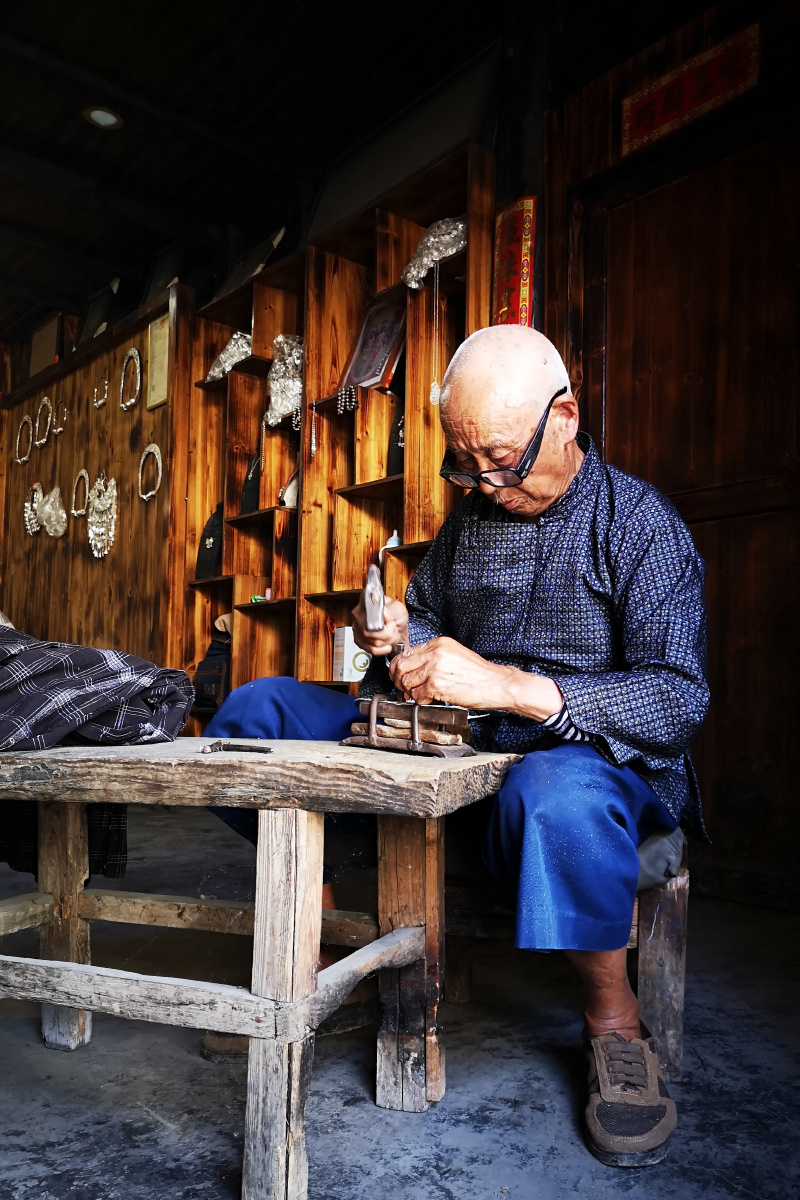 视力日渐衰退的苗族老银匠,靠着门口射入的光线,全神贯注打制着银项圈