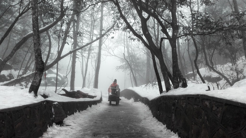 摄于张家界天门山，这天雾很大，夹着小飞雪，路面很滑，不小心摔了一跤以后坐在路边休息，回头看见这位工人正坐在运送木头的小推车上休息，并从兜里拿出一块干粮放在嘴里啃着~~~~这样的天气在山上劳作.....他们辛苦了！