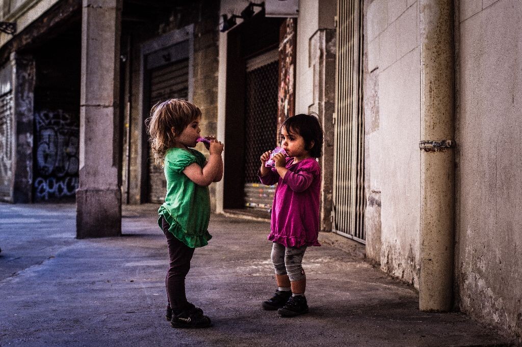 巴塞罗那哥特区的小巷子里，两个小女孩正在吸食着果冻。她们的父母正在不远处的街边坐着享受他们的午后闲暇时光，一切都是那么安静和美好。<br />
