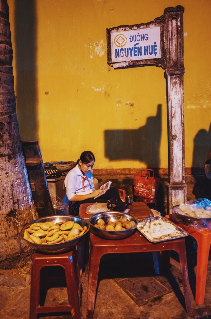 会安古城，昏黄的路灯下，喧闹之中，一个女学生在自家的摊位旁静静滴看着书。2015.12.1 RICOH GR