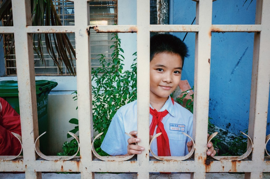 用相机在学校门口扫街的过程中，我们发现一个男孩子透过栏杆想买路边摊的零食。他发现了我们对准他的镜头，也没有跑掉，而是羞涩地微笑起来。<br />
2015.12.2 RICOH GR