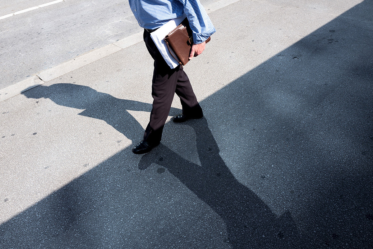 人行道上一个男子走在阴影的边线上.