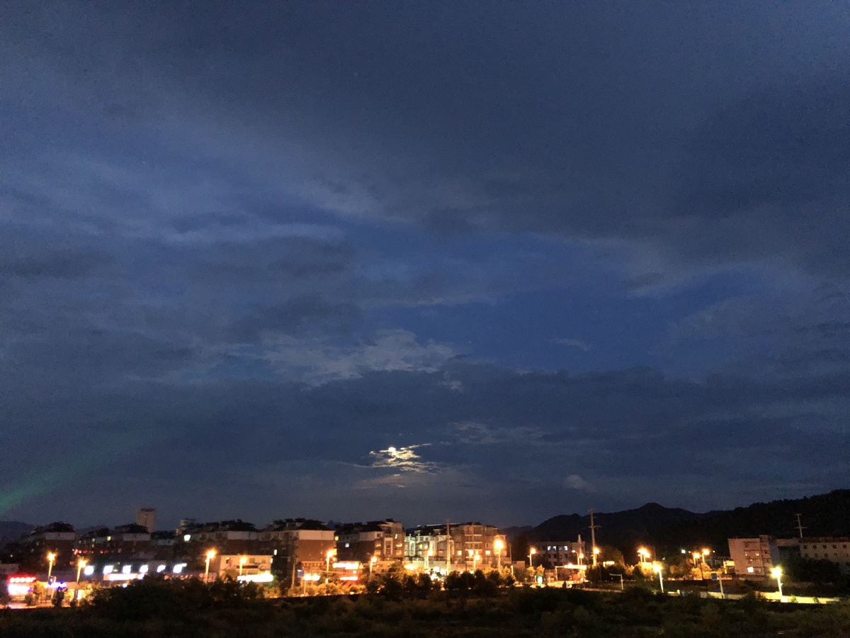 夜幕低垂,天空中的月亮半遮半掩,城市的灯光让这静谧的夜晚更