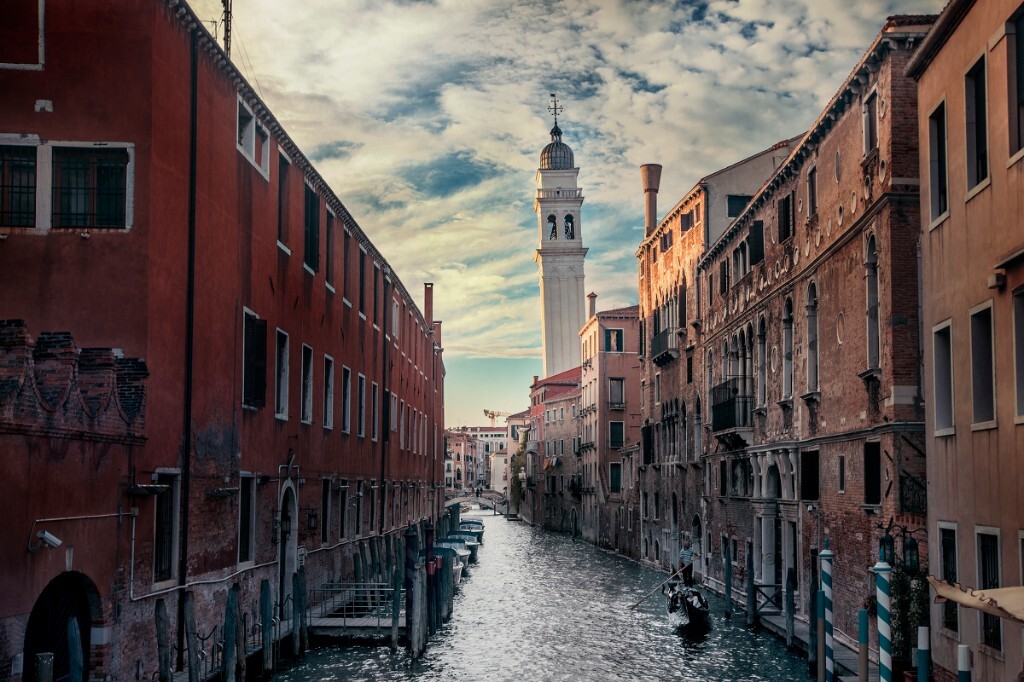 落日照耀倾斜的钟塔，从旁平静的水，贡多拉穿过古老的水道。Venice