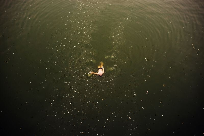 一男子从满是漂浮物的河面游过。