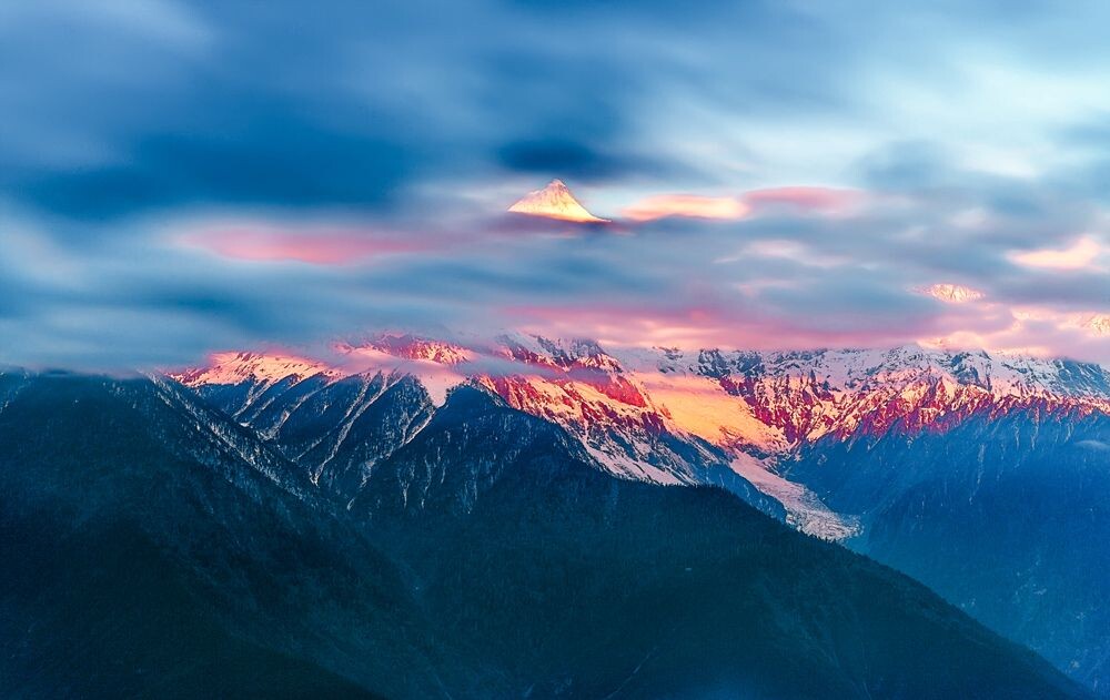 初升的太阳照在浓云密布中偶露一点山峰的梅里雪山,分外梦幻