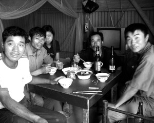 拍摄于2006年10月15日，湖北省武汉市汉阳区，汉蔡高速公路1标。几位工人围在一起吃晚饭，因为天气热，加上工作劳累，晚饭会喝点冰镇啤酒解乏。他们几个都是同村的，还有一对夫妻，所以他们开“开小灶”自己做饭，以改善伙食；桌子是利用工地上的废旧材料自己制作成的。