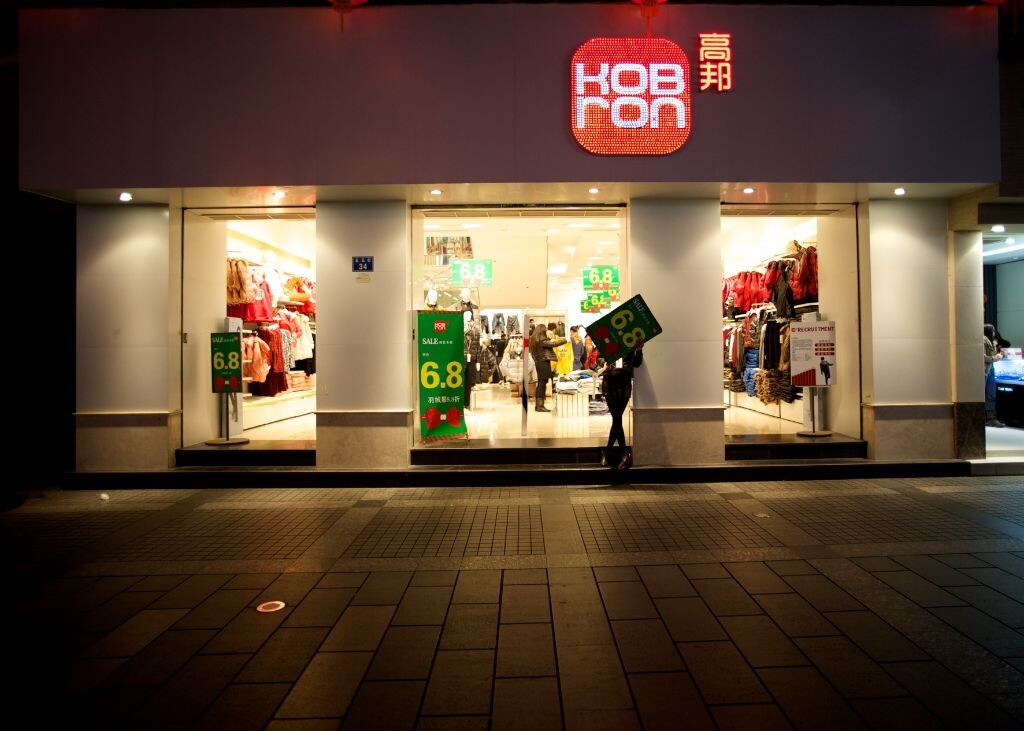 一服装店正在打折,营业员站拿着打折的广告站在门口招揽顾客。
