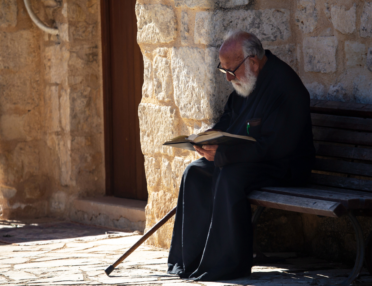 一位神父走出教堂,坐在教堂外面的椅子上看书.