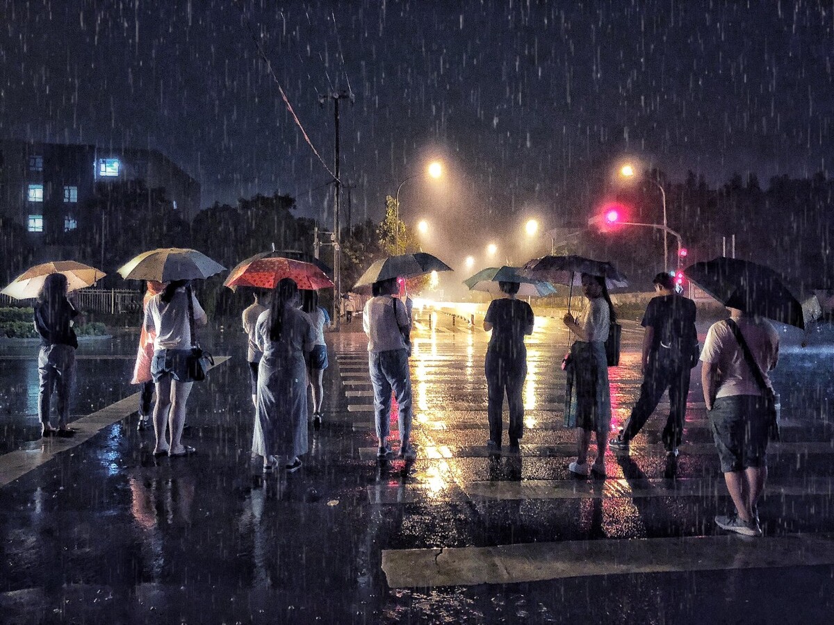 下班后的雨夜,人们站在斑马线上等着红绿灯,准备过到马路对面做一