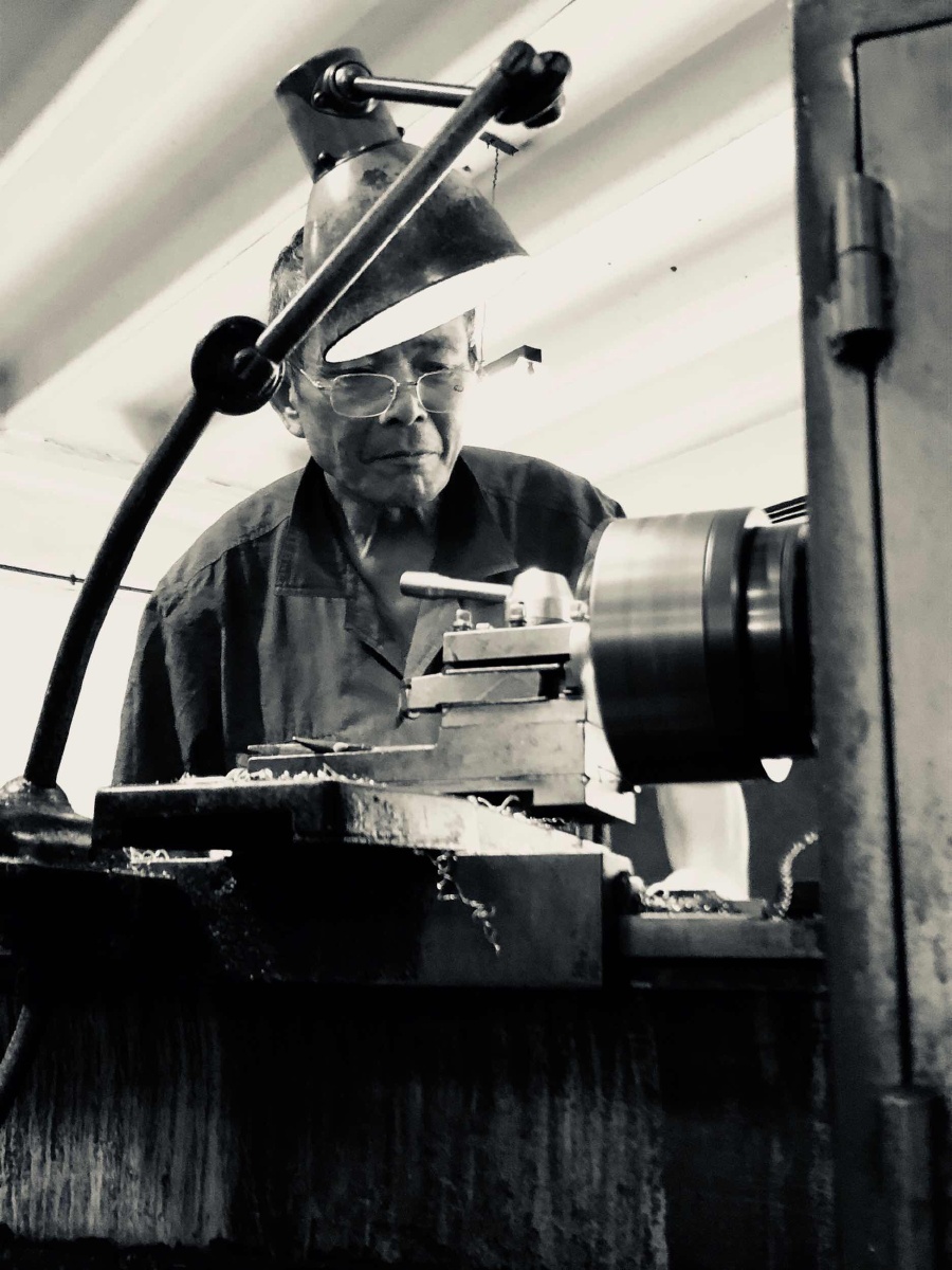一个老工人一丝不苟的在台灯下的金属机器前做事 整个车间里也只有他