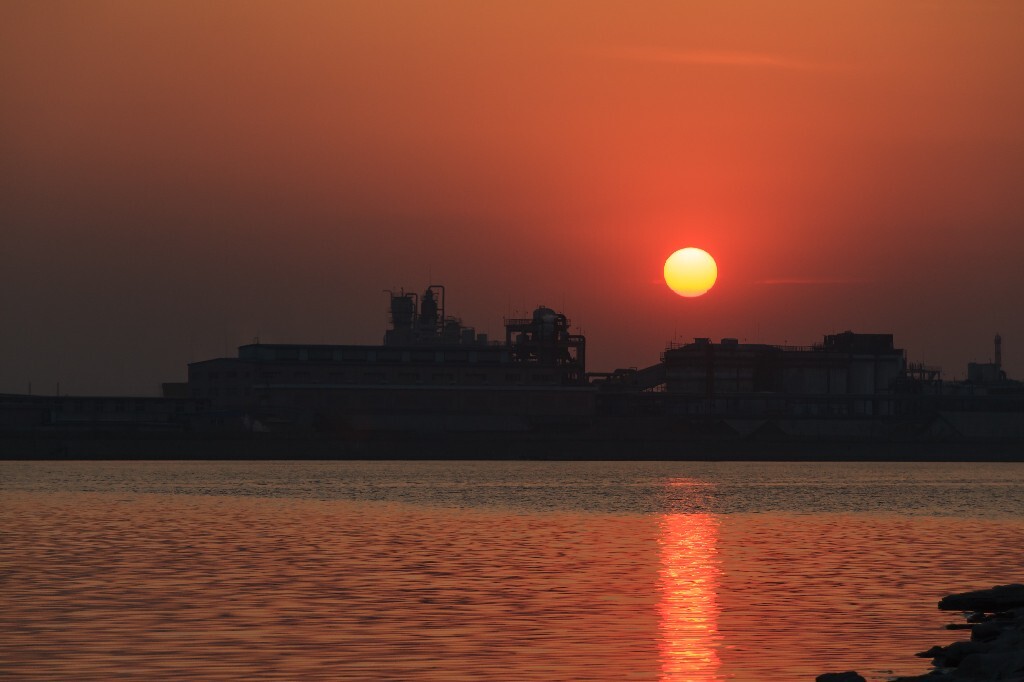 河边公园对岸，即将落下的夕阳笼罩着老旧的化工厂……