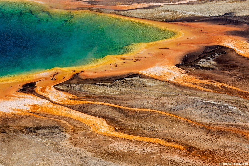 The Grand Prismatic Spring in Yellowstone National Park. 大棱镜温泉也是黄石公园里最有名的间歇泉之一。大棱镜温泉的美在于湖面的颜色随季节而改变，春季，湖面从绿色变为灿烂的橙红色，这是由于富含矿物质的水体中生活着的藻类和含色素的细菌等微生物，它们体内叶绿素和类胡萝卜素的比例会随季节变换而改变，于是水体也就呈现出不同的色彩。