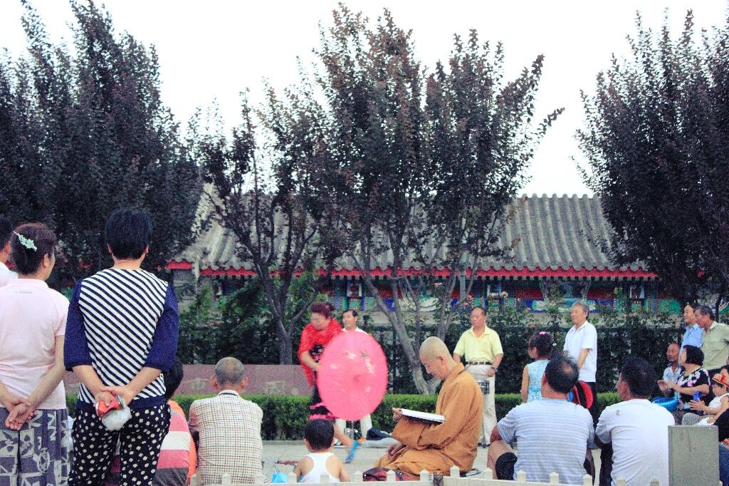 北京雍和宫外，在一群跳舞老阿姨中，一位出家人在专心地看书。