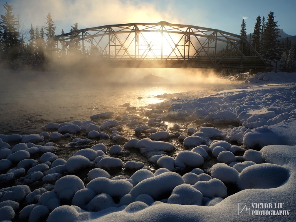 隆冬时节，加拿大落基山，班夫国家公园，这座铁桥跨跃的河流是弓河，在那上面还有一只鹰的巢穴，静悄悄的，太阳升起来将雾气点燃，和着水中星星点点的雪馒头，还有一丝不挂的天空，加拿大隆冬进行时。