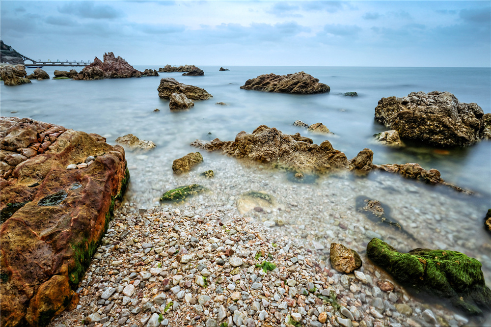 动转为静,这记录着岁月痕迹的礁石跟平静透明的海面如同一个冷酷仙境