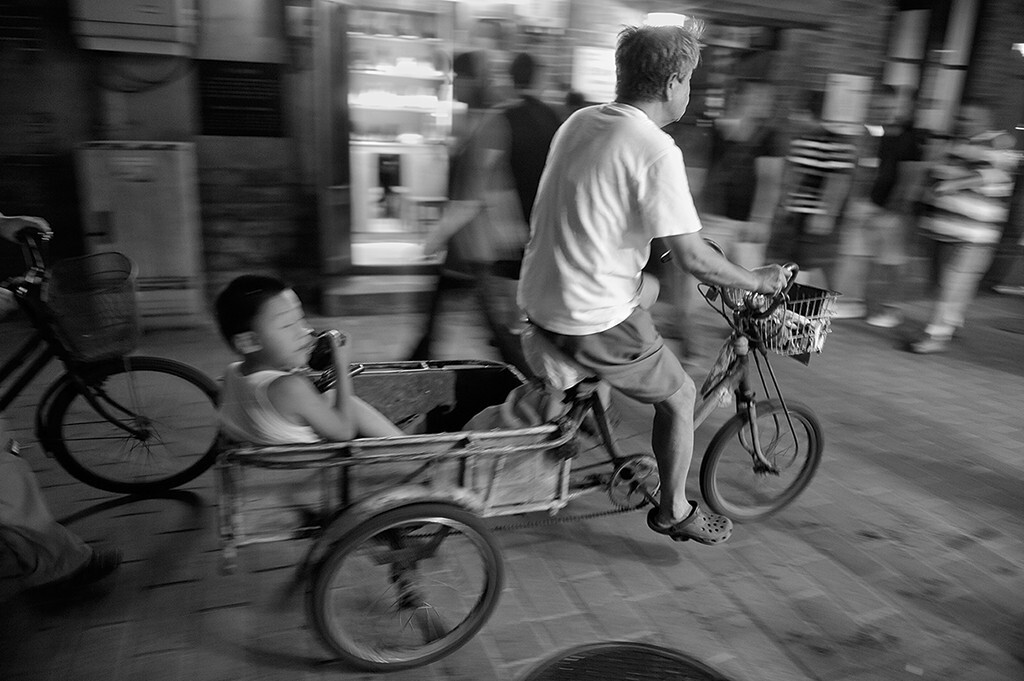 巷子里不时穿梭过小三轮脚踏车，骑车的长辈总是那般沧桑，目不斜视，被生活折腾得麻木了，而孩子坐在车斗里总是左顾右盼，好奇无比。