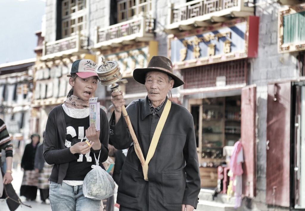 该张照片拍摄于西藏拉萨。在八廓街上，正在转经的爷爷认真的听孙女讲故事。