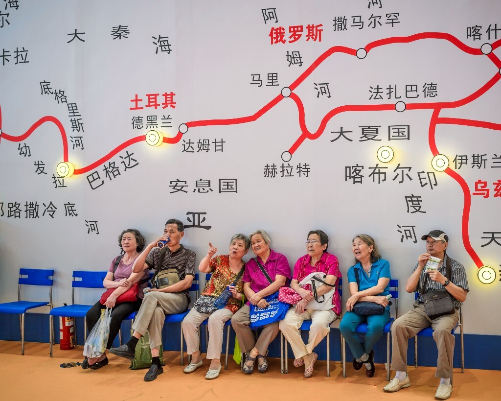 在第八届中国西部文化产业博览会上，7位退休职工坐在丝绸之路巨幅地图前，欣赏一带一路人文风情展示，商讨计划中的丝路之旅。
