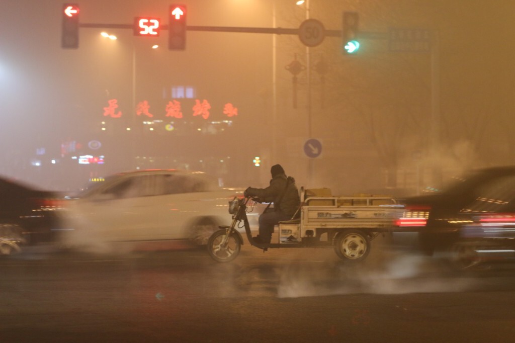 20151223，秦皇岛，21:00，重度雾霾，空气质量指数242，十字路口一位骑着电动三轮车的人在路中间等待转弯，远处烧烤店的招牌穿过雾霾更显醒目，在他周围汽车排出的尾气形成一团团的烟雾。原创，拒绝后期制作。