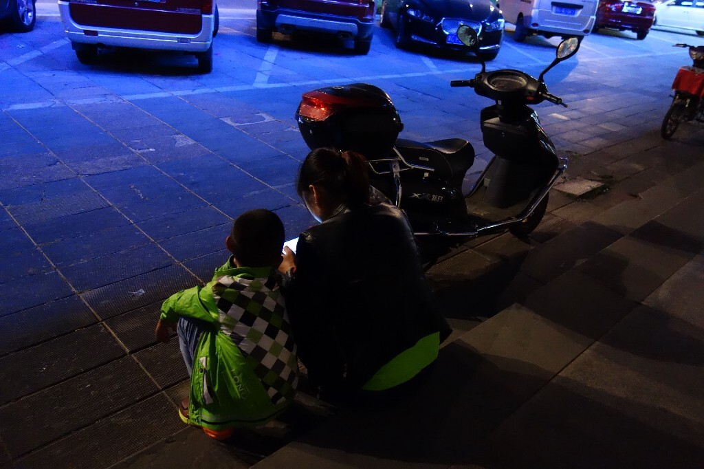 20150909,秦皇岛,夜晚做在路边的一对母子,妈妈在打手游,儿子专心的看着。
