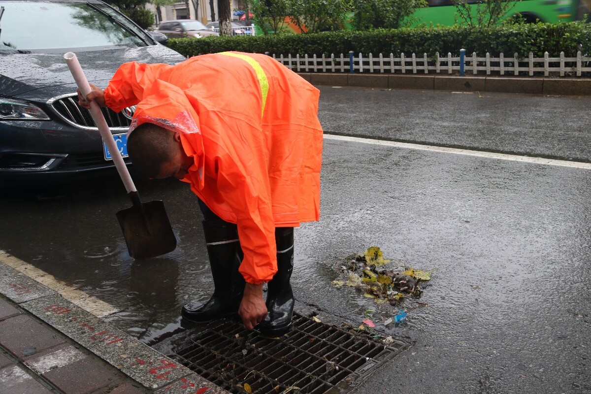 一位环卫工人在雨中抓紧清理下水道入口，防止随雨水而来的落叶等杂物堵塞入口，影响排水。原创，拒绝后期制作。