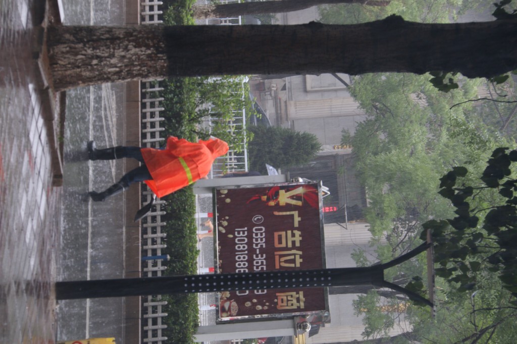 急着清理下水道入口的清洁工人清理完一个冒雨跑向下一个。