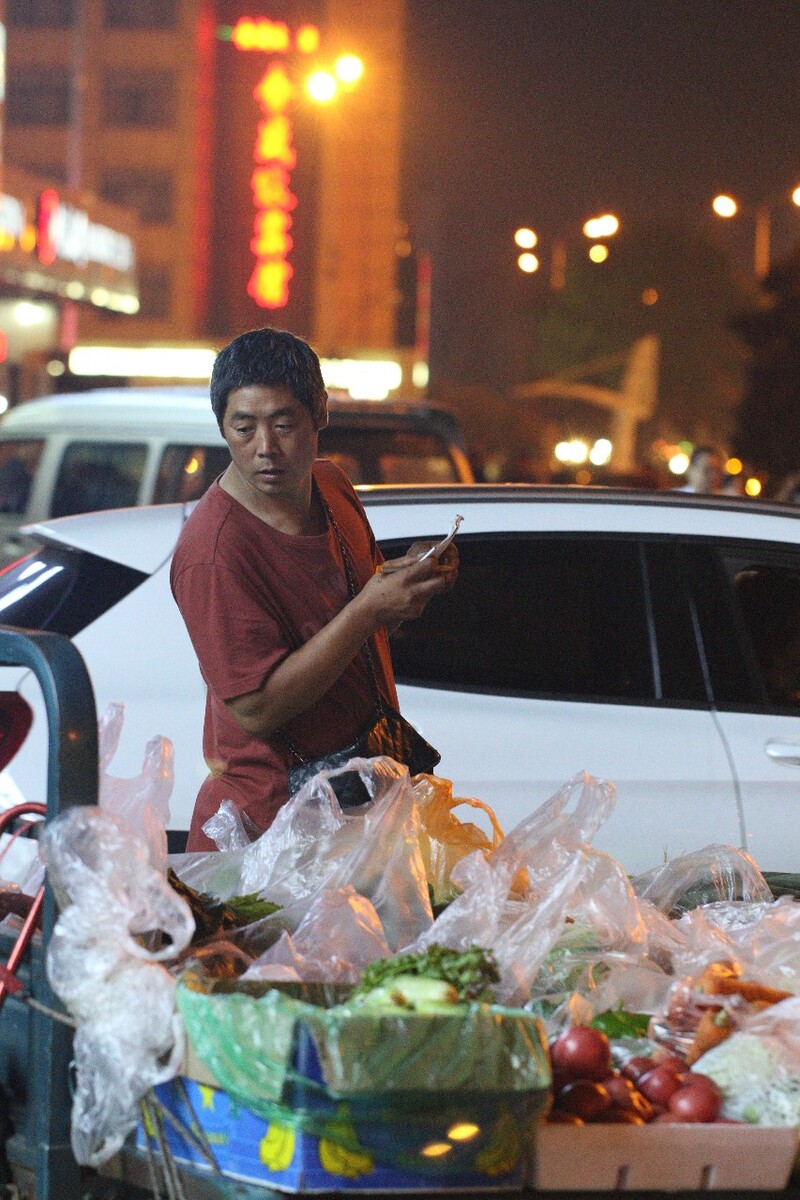 夜晚路边卖菜的师傅在盘点一天下来那些菜卖的好，然后登记到小本子上，计划好明早去批发市场进菜的清单。原创，拒绝后期制作。