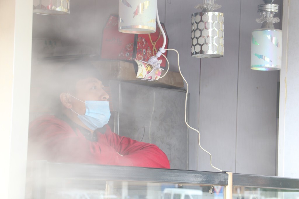 一家糕点铺子临街开放的售货窗口前，一位糕点师在闲暇时趴在货柜上用手机看视频，隔壁包子铺刚熟了一屉包子，热腾腾的蒸汽弥漫过来，几乎遮住了他，但他仍看的津津有味。原创，拒绝后期制作。
