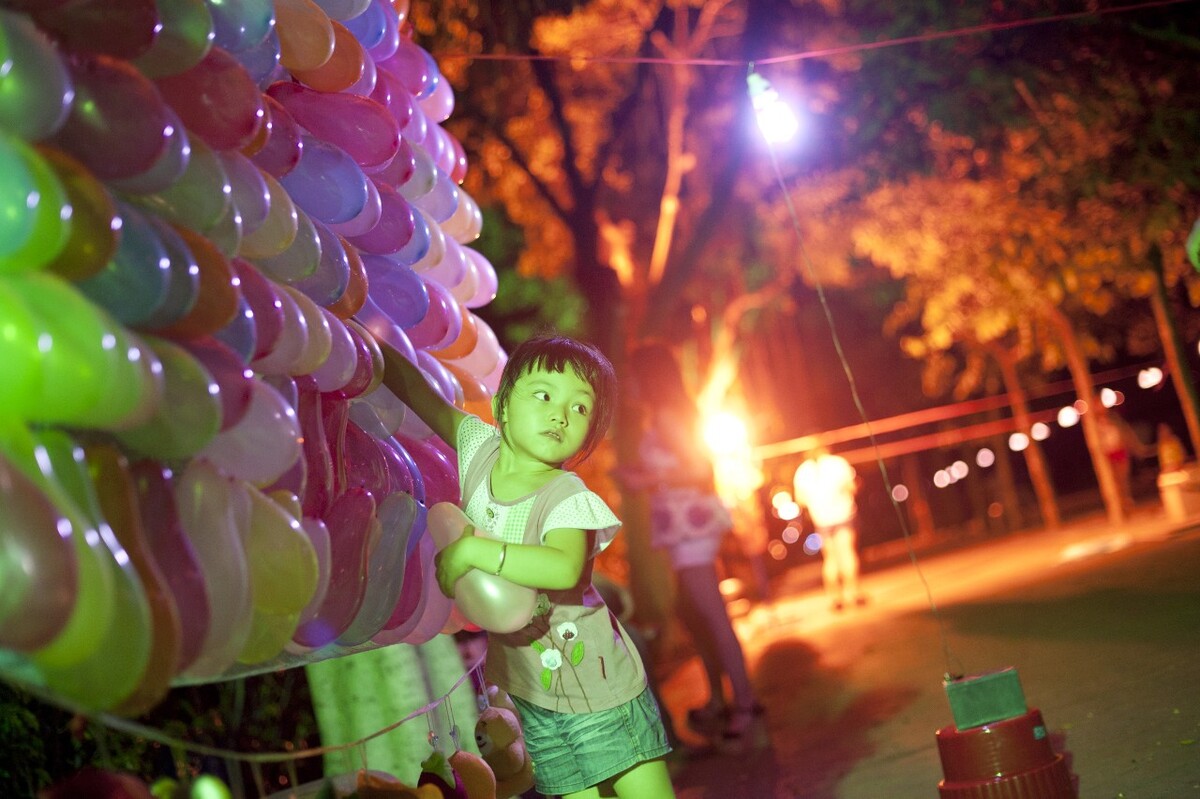 2013年7月31日,广州市员村江边广场。每逢暑假,操着各种口音的人逐渐多了起来,外来务工者会把子女接到广州相聚。四岁的小莉在珠海上幼儿园,暑假她来与在广州工作的妈妈相聚。夜晚,小莉帮妈妈在江边广场布置供游人消遣的游戏摊位。