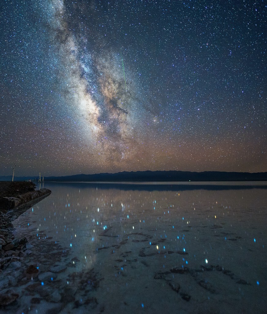 英仙座的绿色流星划过银心，倒影在茶卡盐湖的水面上。水底是之前的游人用石子摆出的“LOVE&quot;