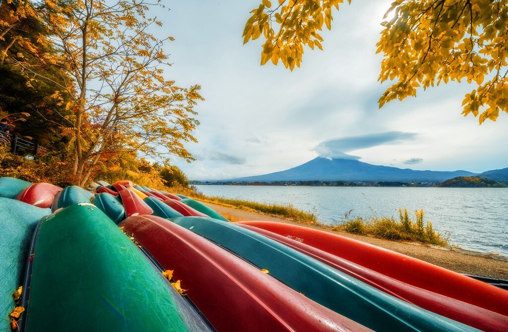 山梨县河口湖，湖畔艳丽的皮划艇。富士山顶藏在盘旋的荚状云中。